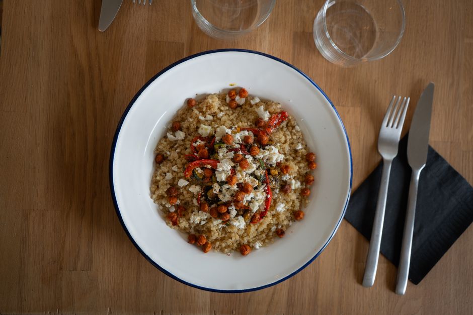 Top view of a quinoa salad with chickpeas, red peppers, and feta cheese on a wooden table.