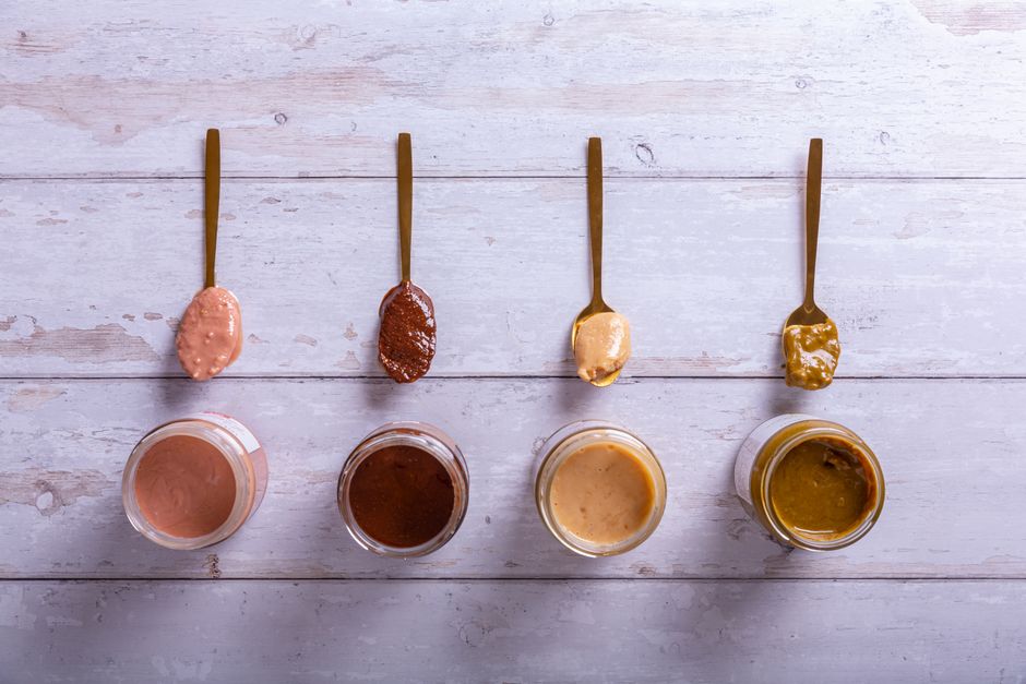 Top view of various nut butters in jars and spoons on a wooden surface.